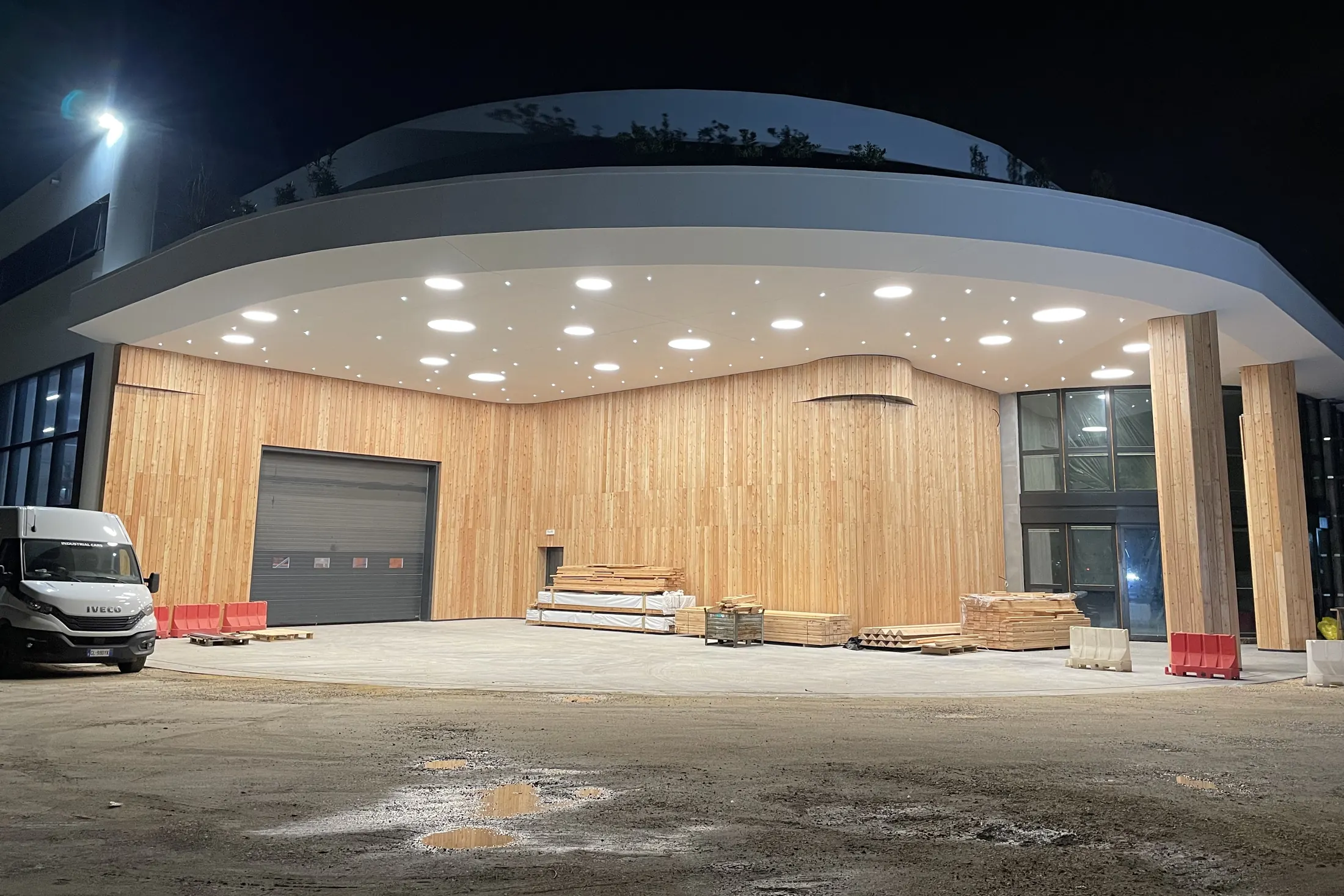 Edificio commerciale illuminato di notte, con grande copertura curva e facciata in doghe di legno realizzata da GSM in provincia di Vicenza