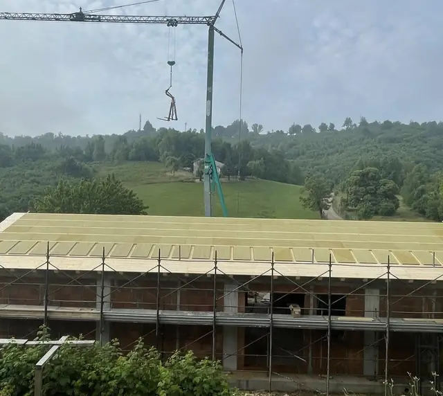 Gru edile posa i pannelli di copertura in legno sul tetto di un edificio in laterizio
