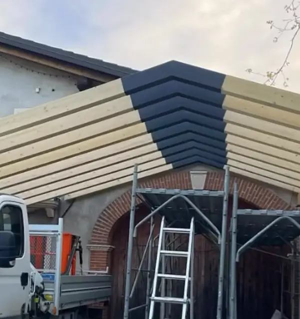 Tettoia con travi in legno e colmo in metallo nero su edificio storico in mattoni